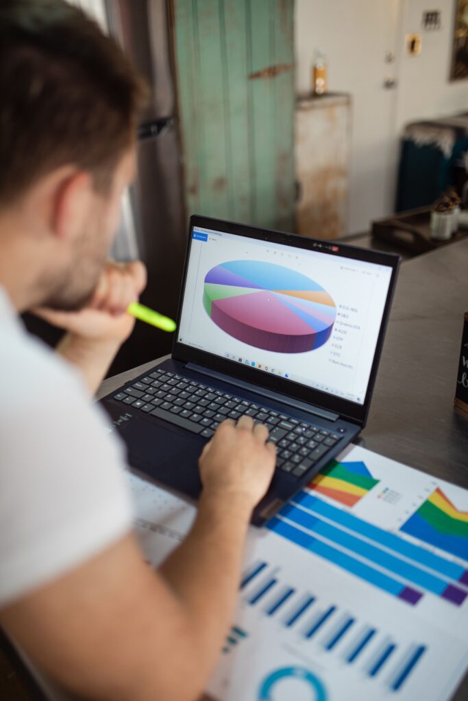 Person reviewing a pie chart on a laptop beside printed charts.
